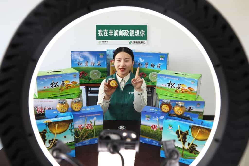 Mujer promociona productos agrícolas y frascos de miel en evento en China, con cajas y paquetes de productos naturales.