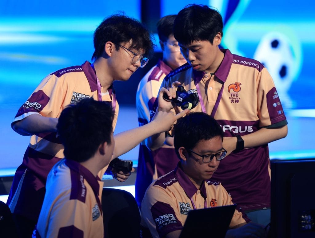 Jóvenes programadores trabajan en un torneo de robótica con concentración y tecnología avanzada.