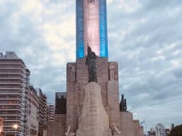 Grupo de jóvenes y adultos en Plaza de la Bandera, Resistencia, con la Torre Monumental iluminada al atardecer.