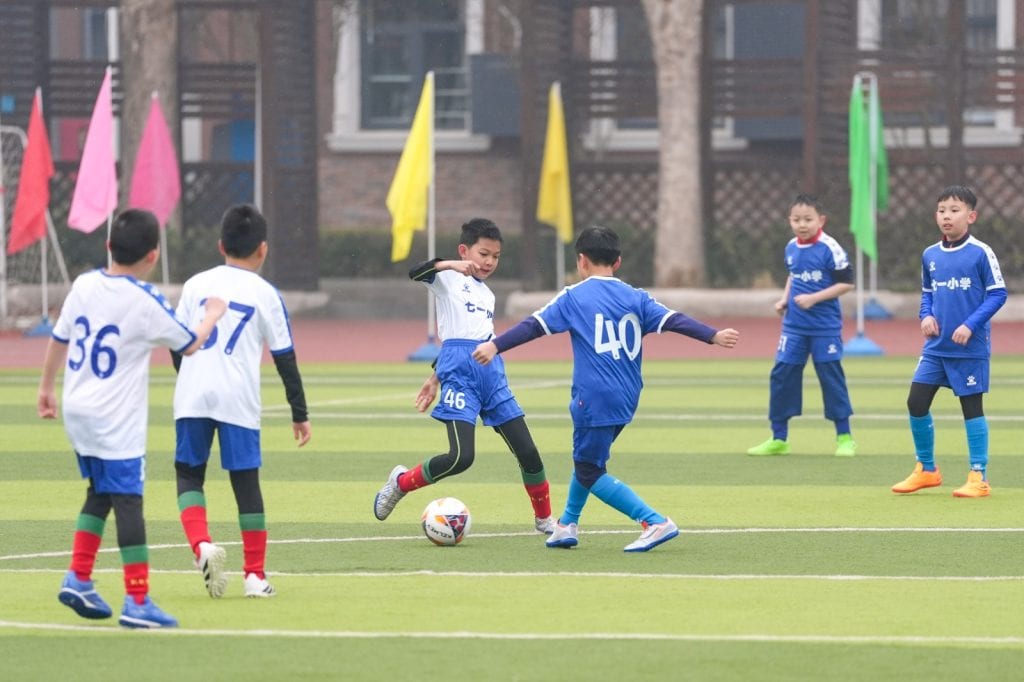 Niños jugando al fútbol en cancha escolar durante actividad deportiva
