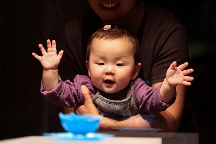 Bebé en China abriendo las manos alegremente mientras recibe el cuidado de sus padres.