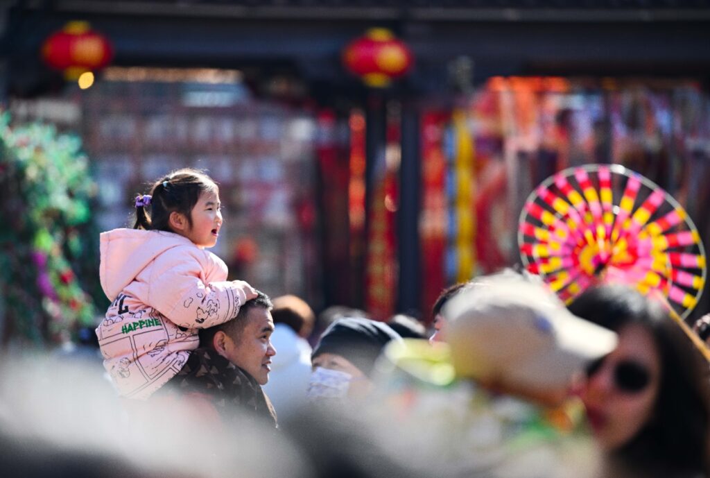 Niña sonriente en los hombros de su padre durante una festividad tradicional en China.