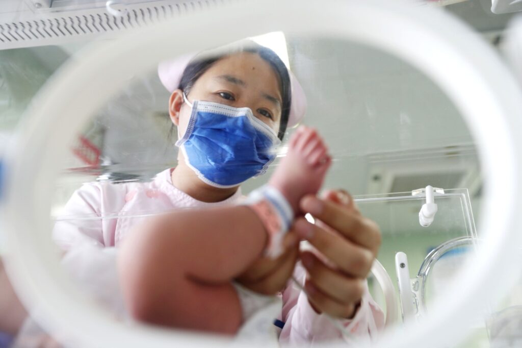 Personal sanitario examinando a un recién nacido a través de la portañuela de una incubadora médica en China.