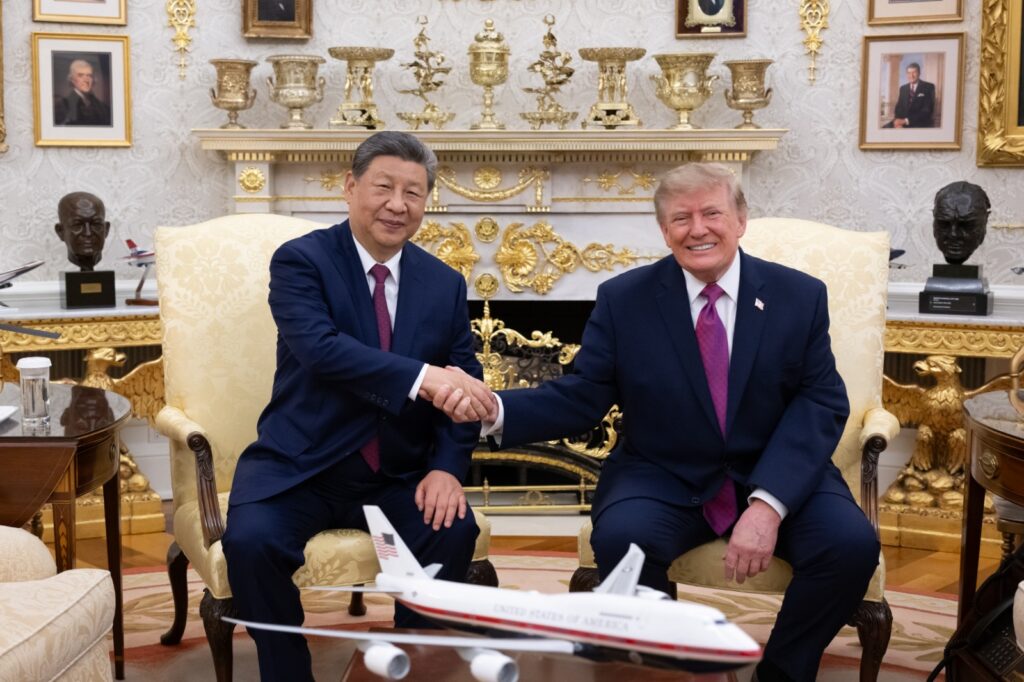 Xi Jinping y Donald Trump estrechando manos en el Despacho Oval con la maqueta de un avión presidencial en primer plano.