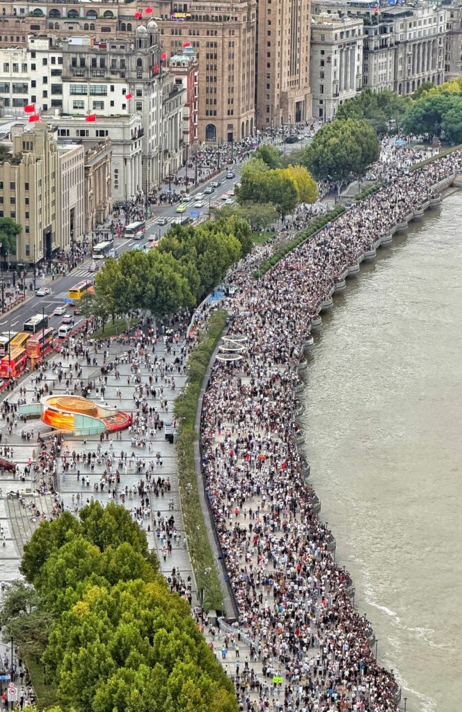 Vista aérea del paseo marítimo El Bund en Shanghái repleto de miles de turistas caminando a lo largo del río Huangpu frente a edificios de arquitectura histórica.