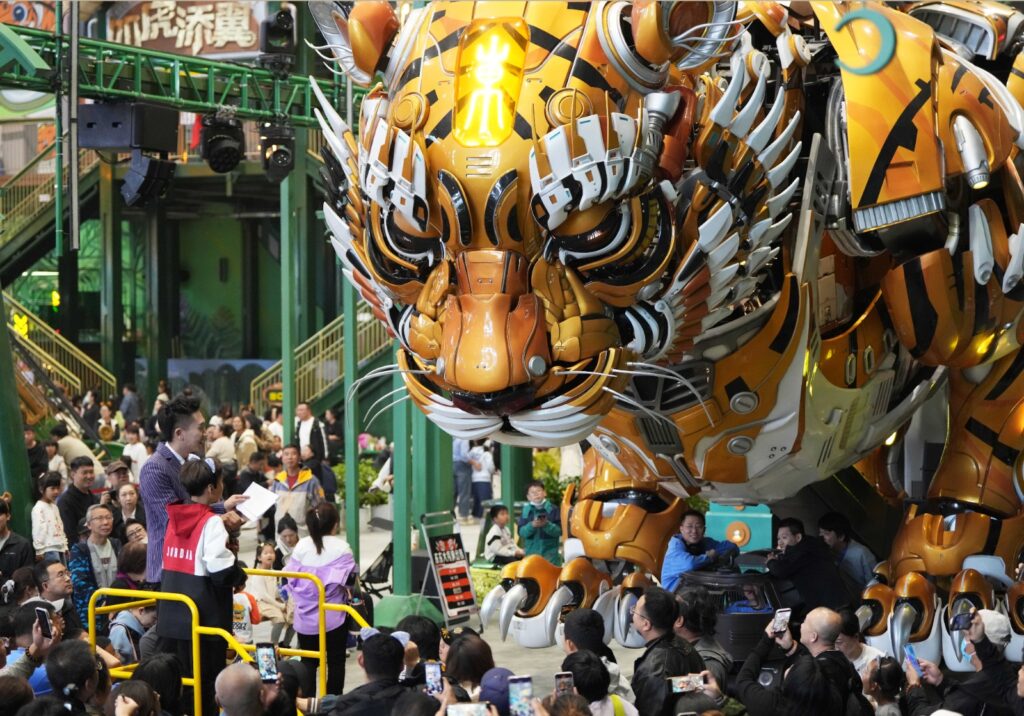 Gigantesca escultura robótica animatrónica de un tigre dorado siendo fotografiada por una multitud de visitantes en un parque de atracciones en China.
