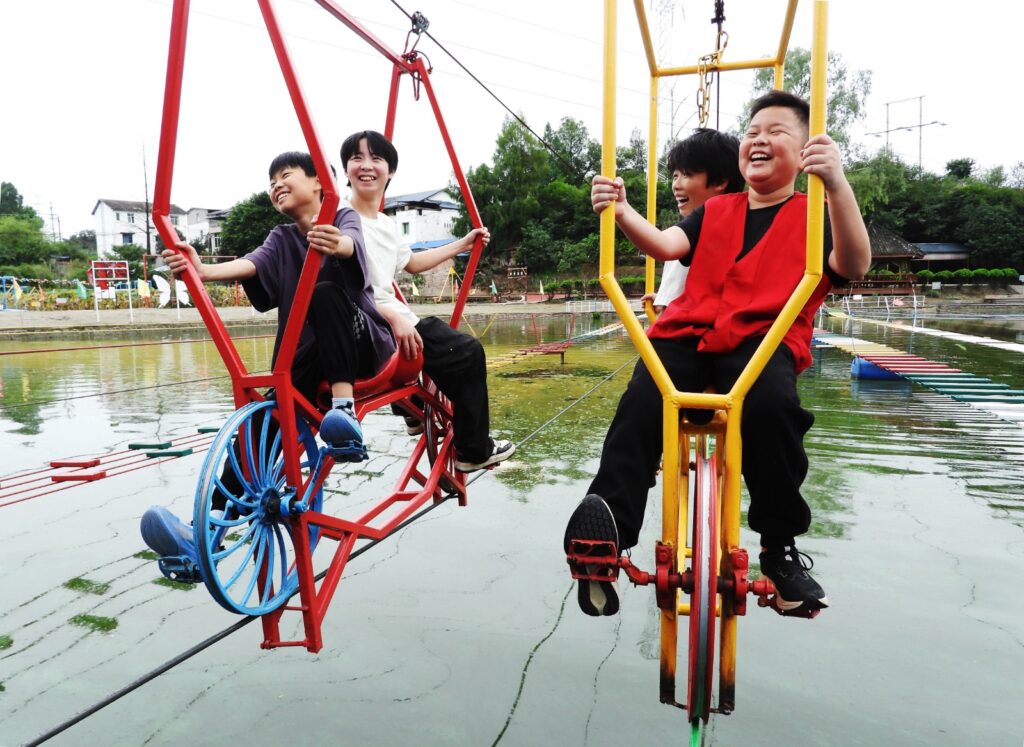 Cuatro niños sonrientes paseando en bicicletas aéreos suspendidas en tirolesas sobre un lago en un parque temático en China.
