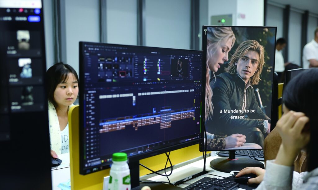 Editora trabajando frente a un monitor vertical que muestra una escena de ficción adaptada con actores occidentales y software de edición.